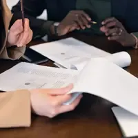 Duas pessoas sentadas a uma mesa de madeira escura, folheando contratos impressos