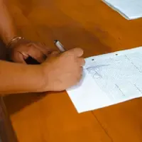 Mão assinando um documento impresso sobre uma mesa de madeira