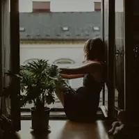 Jovem sentada na porta de uma varanda, ao lado de vasos de plantas