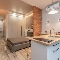 Apartamento pequeno com a cama no mesmo ambiente da cozinha, bancada de madeira com cooktop e parede de tijolo aparente