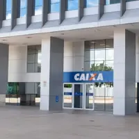 Entrada de uma agência da Caixa Econômica Federal, com letreiro azul sobre as portas de vidro